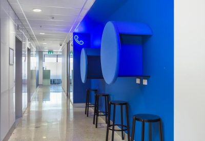 Modern blue corridor featuring integrated acoustic phone booths and stools.