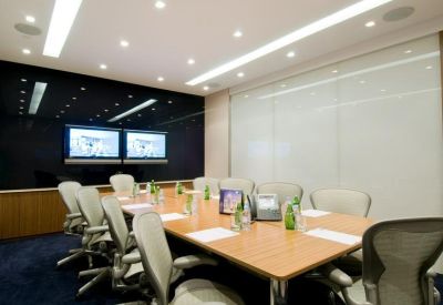 Spacious boardroom with a large wooden table, ergonomic chairs, and dual wall-mounted monitors.