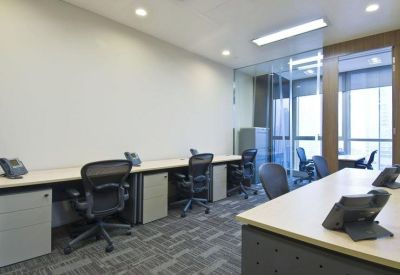 Bright office space featuring long desks with black ergonomic chairs and desk phones.