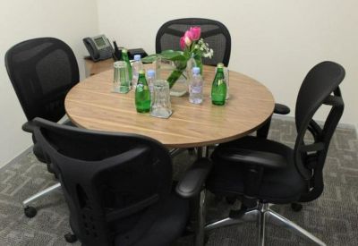 Small meeting room with a round wooden table, four black mesh chairs, and floral centerpiece.