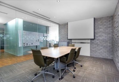 Spacious meeting room with a large rectangular table, olive green chairs, and a projector screen.