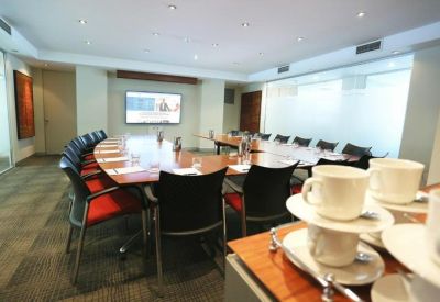 Large boardroom featuring a curved wooden table, red-accented chairs, and a presentation screen.