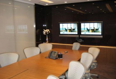 Executive boardroom with dark wood table and dual video conferencing screens.