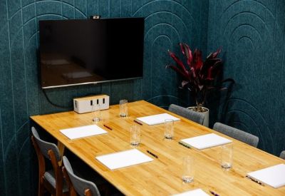 Intimate meeting room with a wooden table, wall-mounted screen, and teal acoustic panelling.
