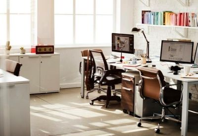 Sunlit open-plan office with white desks and ergonomic brown leather chairs.
