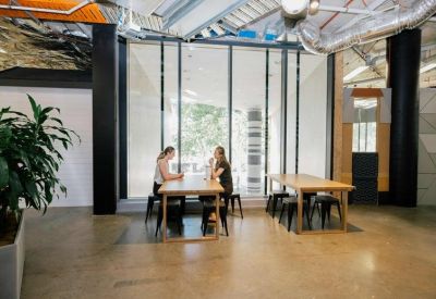 Industrial-style open-plan office with rows of wooden desks and black support pillars.