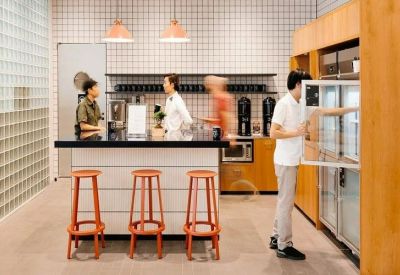 Modern office kitchen area with a white tiled backsplash and orange bar stools.