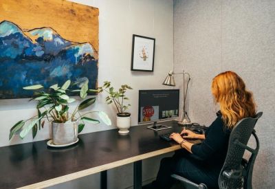Private workstation with a large desk, a computer, indoor plants, and colorful wall art.