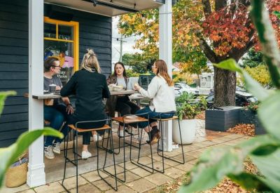 Outdoor patio area with people seated at a high table under a covered porch.