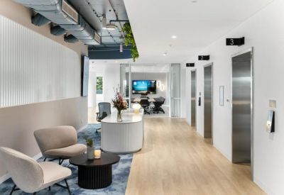 Bright reception area with a white curved desk, comfortable lounge seating, and an elevator bank.