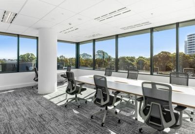 Bright open-plan workspace with white desks and mesh chairs surrounded by large windows.