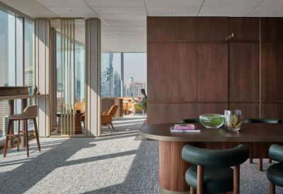 Lounge area with a round wooden table, emerald green chairs, and large windows.