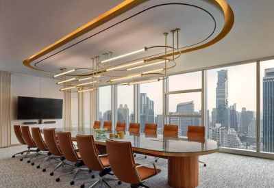 Formal boardroom featuring a long glass table, tan leather chairs, and an oval ceiling light.