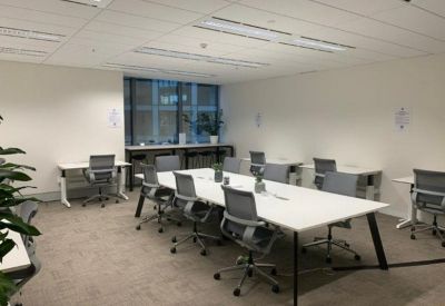 Open-plan workspace with multiple white desks, grey chairs, and bright overhead lighting.