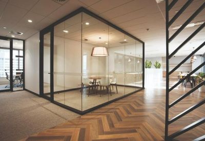 Glass-walled private meeting room featuring a herringbone wood floor and modern light fixture.