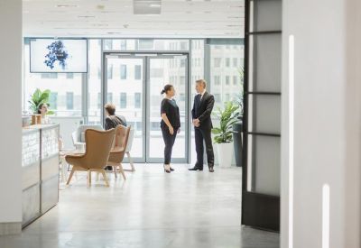 Bright reception area with modern armchairs and staff speaking near large glass doors.