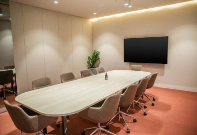 Professional boardroom with a large light wood table, grey chairs, and a wall-mounted screen.