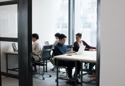 Professional glass-walled meeting room with individuals working at long tables.