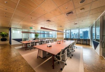 Open-plan office with long wooden desks, ergonomic chairs, and city views.