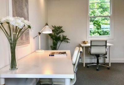 Private office with white desk, task chair, and flowers by a window.