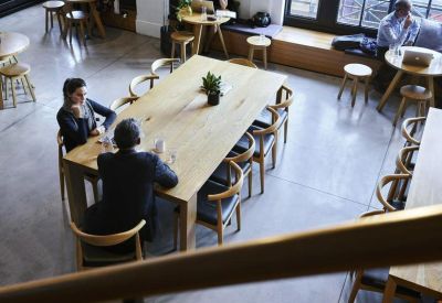 Large wooden communal table in a sunlit breakout area with varied seating options.