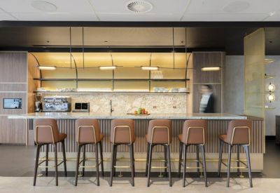 Sleek office kitchen and coffee bar with wooden paneling and brown leather stools.