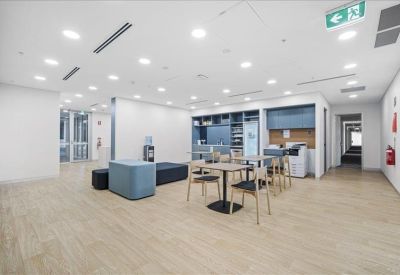 Bright communal break area with modular seating, dining tables, and a kitchenette in the background.