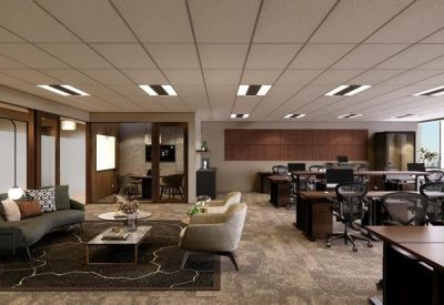 Open-plan office space with dark wood desks, ergonomic chairs, and a cozy lounge area with a sofa.