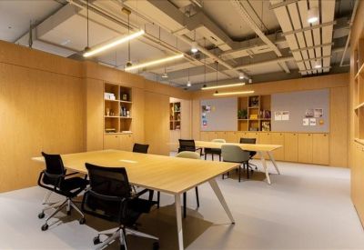 Warm communal workspace featuring wooden wall paneling and several large timber meeting tables.