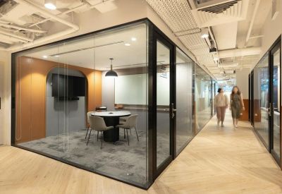 Private glass-walled meeting pod situated along a bright corridor with chevron flooring.
