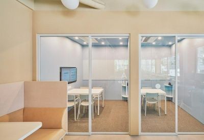 Glass-walled private meeting rooms featuring modern white tables and light wood accents.