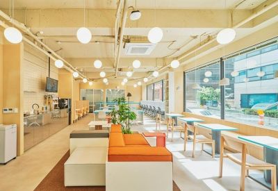 Sunlit coworking space with orange modular seating and small tables by large windows.