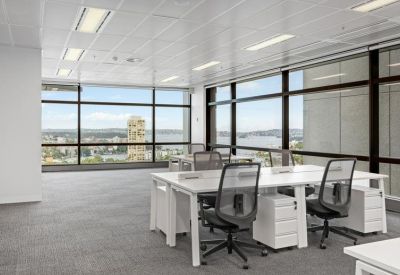 Spacious open-plan workspace with white desks and floor-to-ceiling windows with city views.