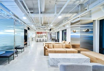 Bright coworking area with tan sofas, marble coffee tables, and glass partition booths.