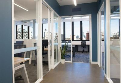 Hallway view showing glass-partitioned private offices and a bright common workspace.