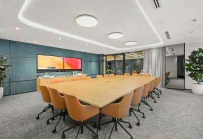 Large boardroom with light wood table, tan leather chairs, and wall-mounted monitors.