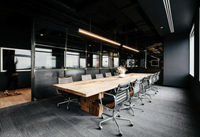 Professional boardroom with a long wooden table, black ergonomic chairs, and mood lighting.