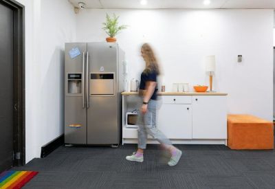 Bright office kitchen area featuring a large stainless steel fridge and white cabinetry.