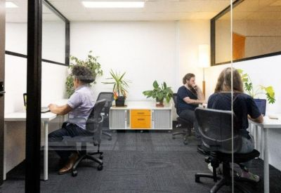 Professional shared office space with multiple workstations, indoor plants, and glass partitions.