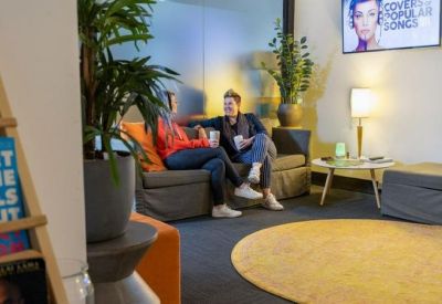 Vibrant lounge area with a grey sofa, orange accents, and a large round yellow rug.