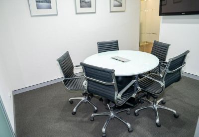 Small meeting room with a round white table and five black leather chairs.