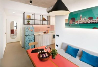Compact studio workspace with a vibrant orange table, blue sofa, and colorful wall art.