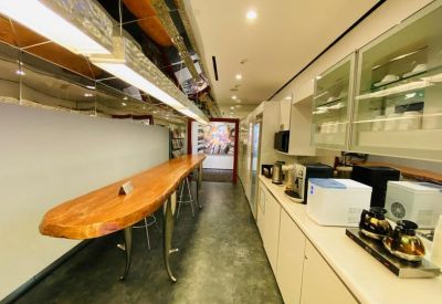 Sleek office pantry with a long wooden breakfast bar and coffee preparation equipment.