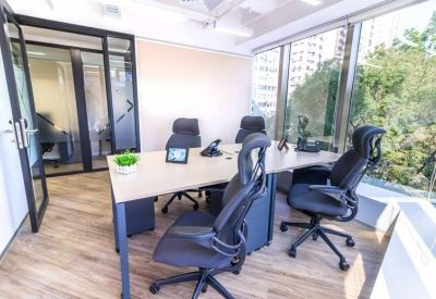 Bright corner office with a large desk and floor-to-ceiling windows showing city trees.