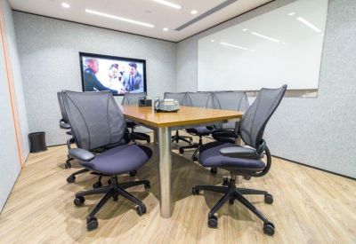 Professional meeting room featuring a dark conference table, grey chairs, and a wall-mounted monitor.