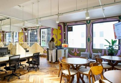 Spacious coworking area with colourful wall murals and round wooden breakout tables.