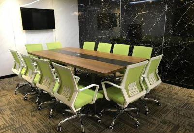 Professional boardroom with a wooden table, green chairs, and a black feature wall.