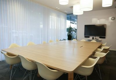Formal boardroom with a large light-wood table, white Eames-style chairs, and a wall-mounted screen.