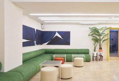 Lounge area with a long green modular sofa, cream-colored ottomans, and bold blue wall art.