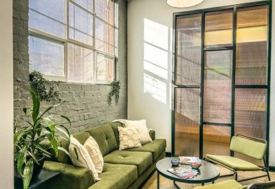 Bright sunlit breakout area with a green velvet sofa and industrial-style windows.
